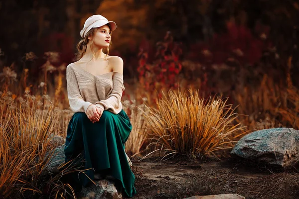Piękna dziewczyna w czapce i płaszczu z gołym ramieniem na tle jesieni — Zdjęcie stockowe