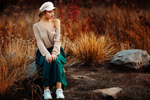 Beautiful girl in a cap and coat with a bare shoulder on the background of autumn — Stock Photo, Image