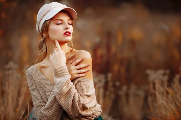 Hermosa chica en una gorra y un abrigo con un hombro desnudo en el fondo del otoño — Foto de Stock