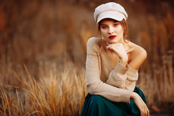 Sonbaharın arka planında çıplak omuzlu şapkalı ve ceketli güzel kız. — Stok fotoğraf