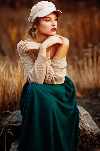 Hermosa chica en una gorra y un abrigo con un hombro desnudo en el fondo del otoño — Foto de Stock