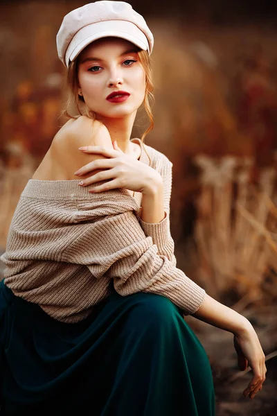 Hermosa chica en una gorra y un abrigo con un hombro desnudo en el fondo del otoño — Foto de Stock