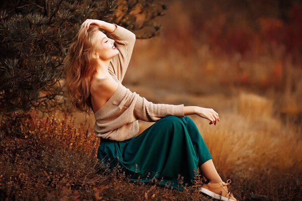 Beautiful girl in a cap and coat with a bare shoulder on the background of autumn walk green skirt, sitting