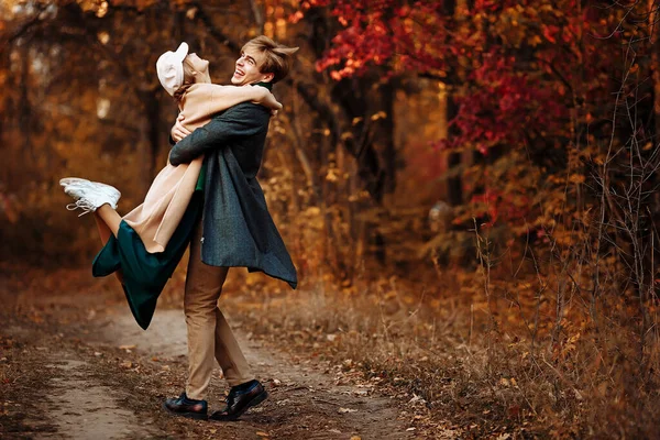 Happy, couple in love hugs and smiles on the street, autumn, green scarf and cap, man and woman on a date. walk in the park under an umbrella in the rays of the setting sun — Stock Photo, Image