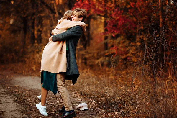 Щаслива, закохана пара обіймає і посміхається на вулиці, осінь, зелений шарф і шапка, чоловік і жінка на побаченні. прогулянка в парку під парасолькою в променях заходу сонця — стокове фото