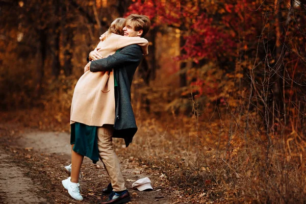 Happy, couple in love hugs and smiles on the street, autumn, green scarf and cap, man and woman on a date. walk in the park under an umbrella in the rays of the setting sun Stock Picture