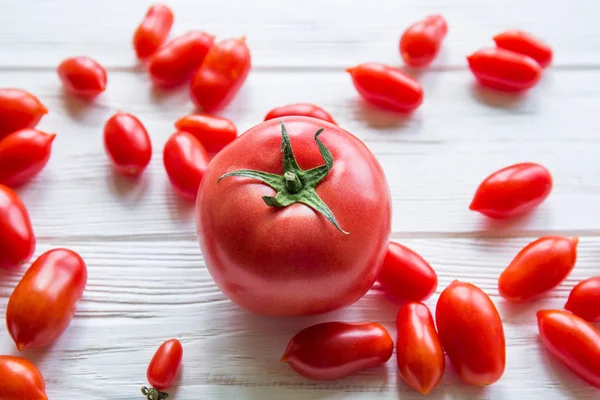 One big tomato with many small tomatoes on white wooden table