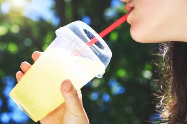 Bir bardak limonata sıcak bir yaz günü bir kız, seçici odak bırakılan cam top elinde sırasında. Yüksek yaz sıcaklıklarda soğuk limonata bardağı taşıran damla içen bir kızın ağzı.