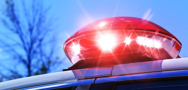 Police car with focus on red siren light. Colorful red siren on the roof of a police car in a real intervention. Beautiful red siren lights activated in full policemen operation. Red light flasher of an emergency car with blue sky background.