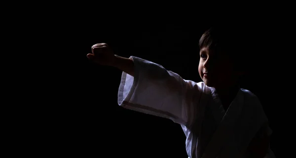 Un niño karate en kimono blanco posando sobre fondo oscuro. Niño listo para la pelea de artes marciales. Lucha de niños en el entrenamiento de Aikido . — Foto de Stock