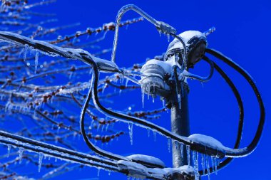 Kablolardan asılı Kristal buz sarkıtları ile elektrik kutusu montajı. Kuzey Amerika 'da hava kış felaketi. Soğuk Kanada baharda buz felaketi. Parlak dondurulmuş arka planda erime saçağı ve düşen parlak damla.