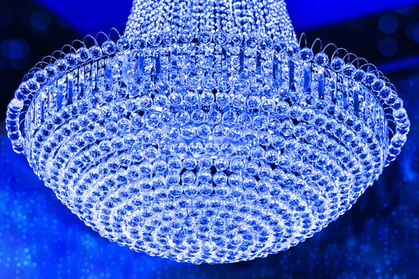 Glow Crystal Lighting or chrome chandelier isolated on blue background. Branched ornamental light fixture. Luxury theatrical chandelier in modern vintage interior.