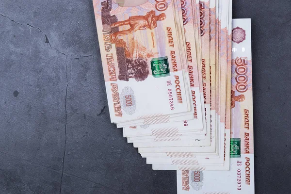 Big stack of Russian money banknotes of five thousand rubles lying on a grey cement background.