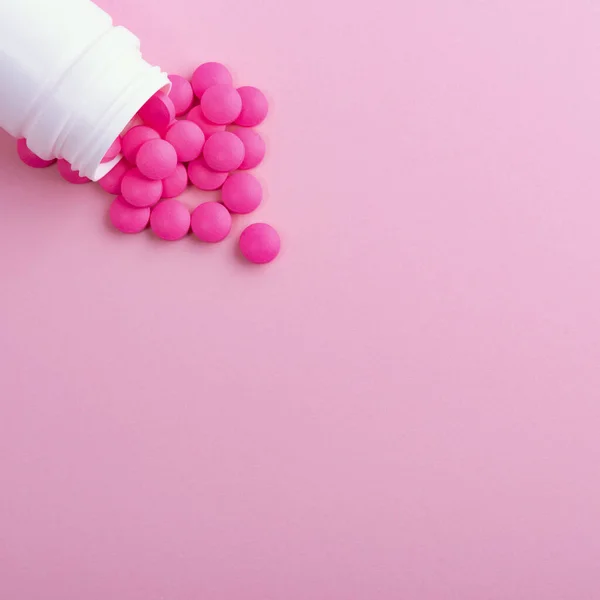 Pills of bright pink color are scattered from a white medical jar. Isolated on a pink background