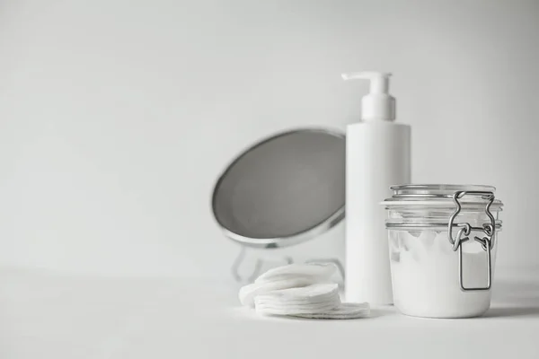 Güzel minimalist kavramsal bembeyaz kompozisyon - Pamuklu ped, şeffaf kavanoz ve plastik şişe ile pompa, yuvarlak ayna, tüm beyaz