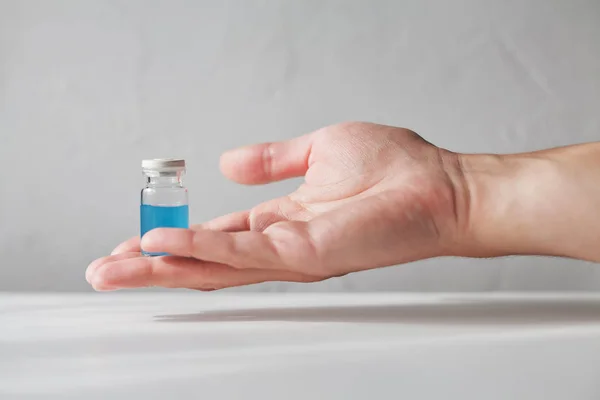 人类的手拿着一个古老的玻璃小瓶充满了青色蓝色液体在白色模糊的背景 — 图库照片