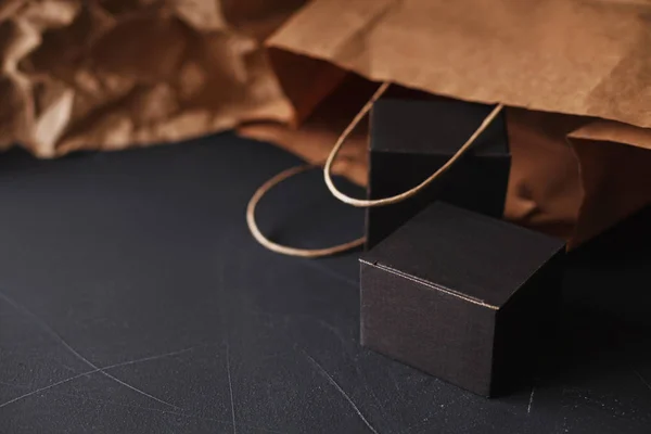 Two matte black carton gift boxes laying on a black painted scratched surface, craft paper bag blurred on background, home gift wrapping craft theme