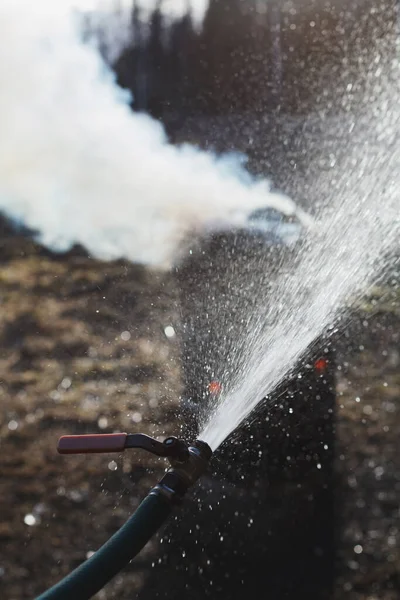 Water spraying from water hose near fire burning in old rusty barrel. Symbol of fire safety.