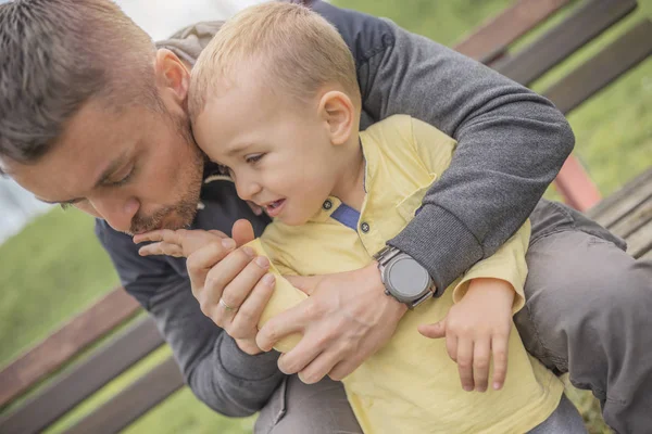 Closeup portrait of a young father and crying kid on playground. Young father hugs crying child. Dad and son.