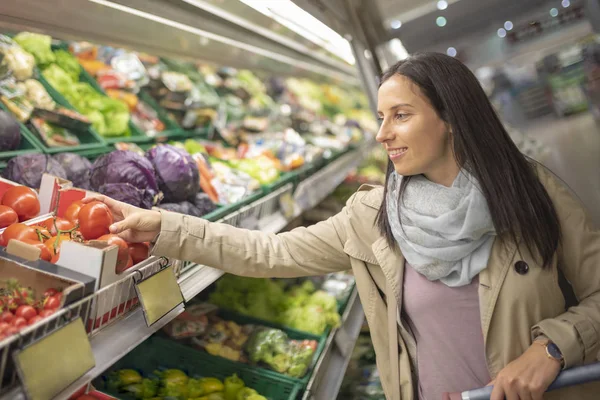 Güzel genç bir bayan marketten yeşil yapraklı sebzeleri seçiyor. Süpermarketten alışveriş yapan çekici bir kadın. Alışveriş yapan kadın sağlıklı yiyecekler alıyor. Sağlıklı yaşam tarzı kavramı.