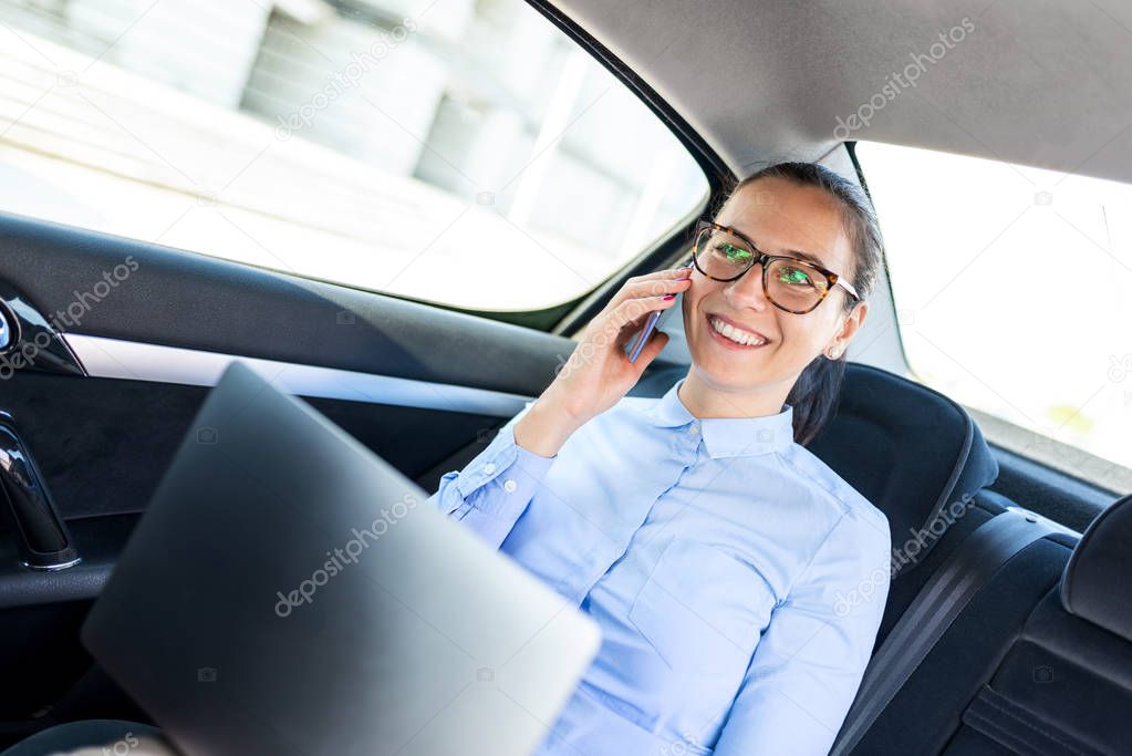 Young businesswoman talking on the phone in the back seat of the