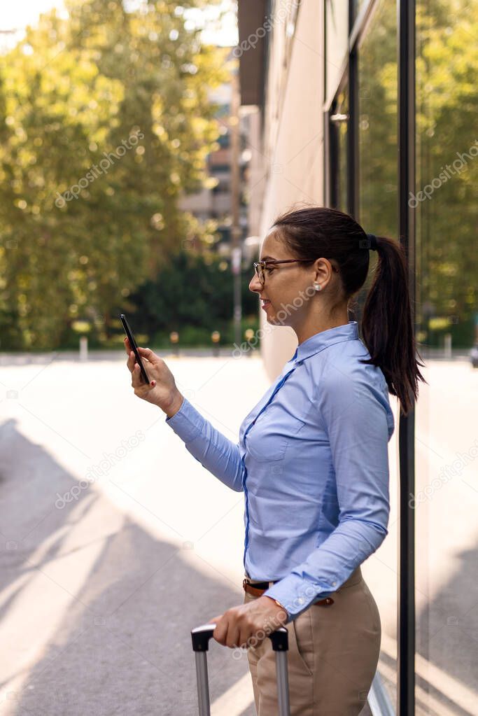 Handsome young woman on business trip walking with her luggage and talking on cellphone at airport. Travelling business woman making phone call