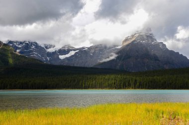 Mavi ve beyaz gökyüzü, dağlar, orman, göl veya nehir ve açık alanları ile Kanada manzara