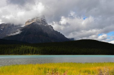 Mavi ve beyaz gökyüzü, dağlar, orman, göl veya nehir ve açık alanları ile Kanada manzara