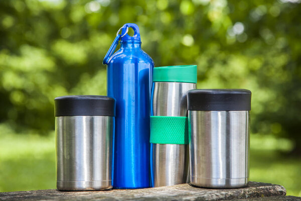 Isolated food and water thermoses on wooden table in nature during daytime