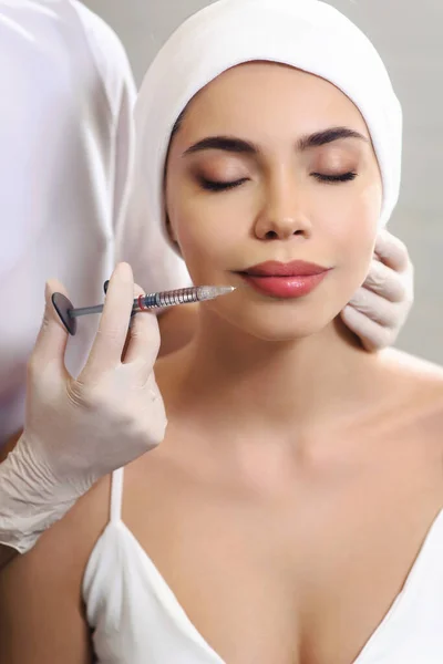 Lips injection close up. Syringe with filler for face contouring or augmentation. Cheerful young woman getting botox procedure. Hands of beautician doctor. Healthcare cosmetology concept.
