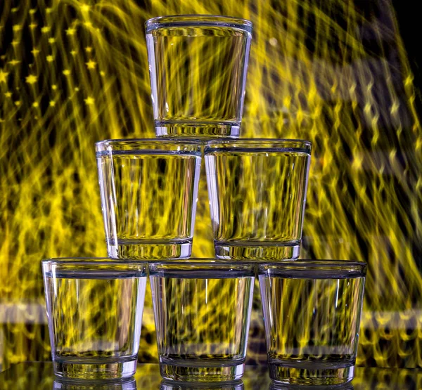 Six glasses stacked by a tower on a multi-colored background