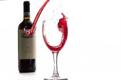 Červené víno spadá do sklenice a vytvoří úvodní a louže na bílém pozadí.
