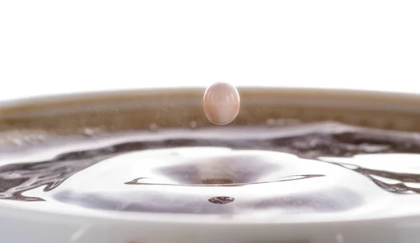 Coffee with cream, splash from a drop of milk on the surface of coffee on a white background