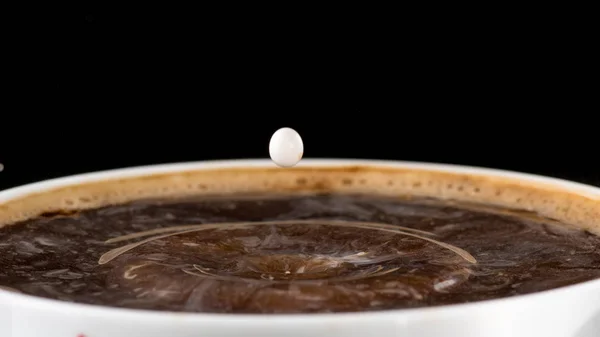 Coffee with cream, splash from a drop of milk on the surface of coffee on a black background