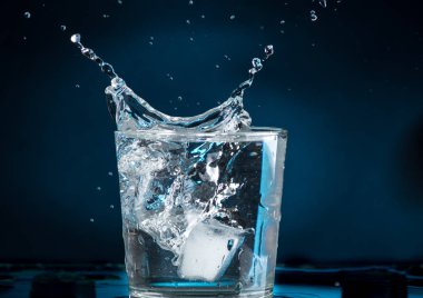 bir bardak su koyu arka plan üzerinde içine düşen bir parça üzerinden sıçrama