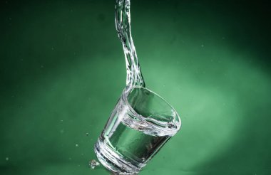 berrak su ve yeşil arka planda su dökülme ile küçük şeffaf cam düşen
