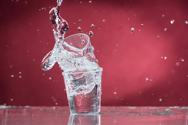 Cayendo Pequeños Vasos Derramando Agua Sobre Fondo Rojo — Foto de Stock