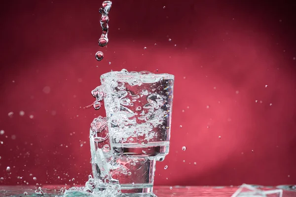 Caindo Pequenos Copos Derramando Água Fundo Vermelho — Fotografia de Stock