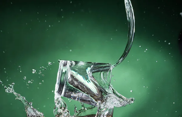 掉落的小透明玻璃与清澈的水和溢出的水在绿色的背景 — 图库照片