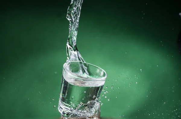 掉落的小透明玻璃与清澈的水和溢出的水在绿色的背景 — 图库照片