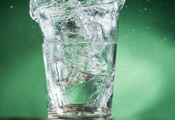Falling Small Transparent Glass Clear Water Spilling Water Green Background — Stock Photo, Image