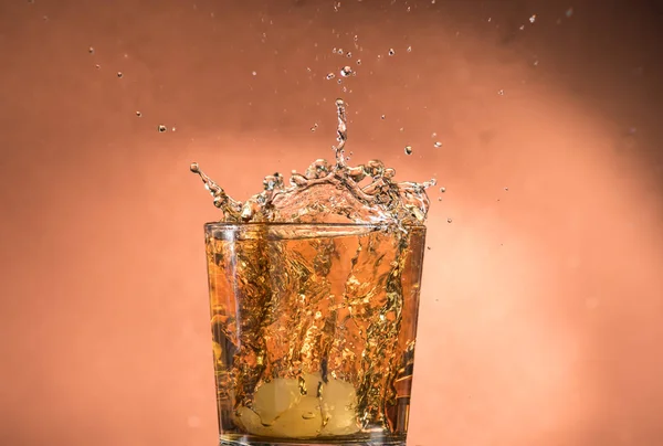Splash Een Glas Whisky Met Ijs Een Oranje Bruine Achtergrond — Stockfoto