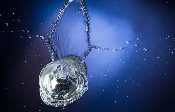 落下とジャンプの青のグラデーション背景に液体をこぼすとガラス — ストック写真