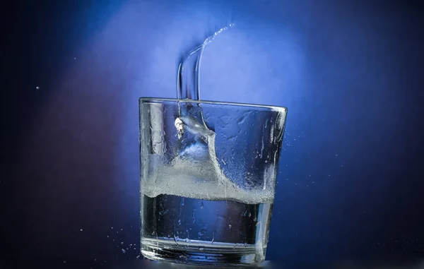 落和跳跃的玻璃与溢出的液体在蓝色梯度背景 — 图库照片