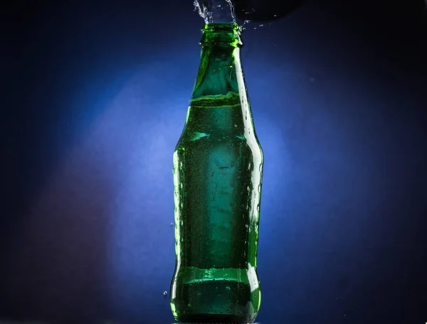Falling and jumping green bottle with spilling liquid on a blue gradient background