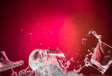 düşen ve cam smashing uçan cam votka kırmızı degrade arka plan, parçaları ve sıçraması için vurdu