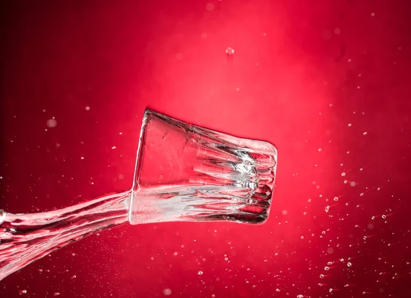 flying falling and smashing glass shot glass for vodka on a red gradient background, fragments and splashes