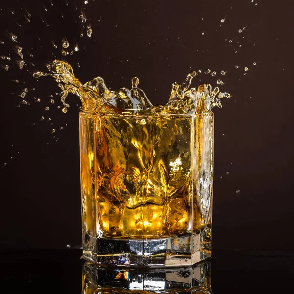 hexagonal glass of whiskey with ice and splashes from an abandoned and falling ice cube