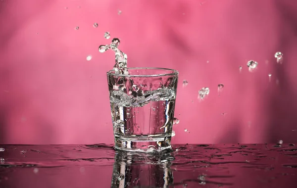 Glass with vodka and a big splash on a colored background