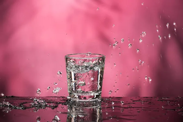 Glass with vodka and a big splash on a colored background